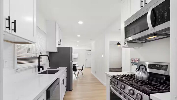 A modern kitchen with white cabinetry, a stainless steel stove, and a microwave.