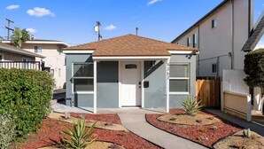A modern two-story house with a covered patio, a front yard with red mulch and plants, and a wooden fence.