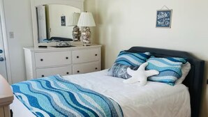 A bedroom with a bed, a dresser, a mirror, and a wall sign.