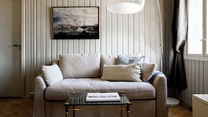 Un salon avec un canapé, une table basse sur laquelle repose un livre, un luminaire suspendu et un tableau encadré accroché au mur.