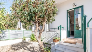 Un edificio bianco con una porta verde, una scala e un albero sullo sfondo.