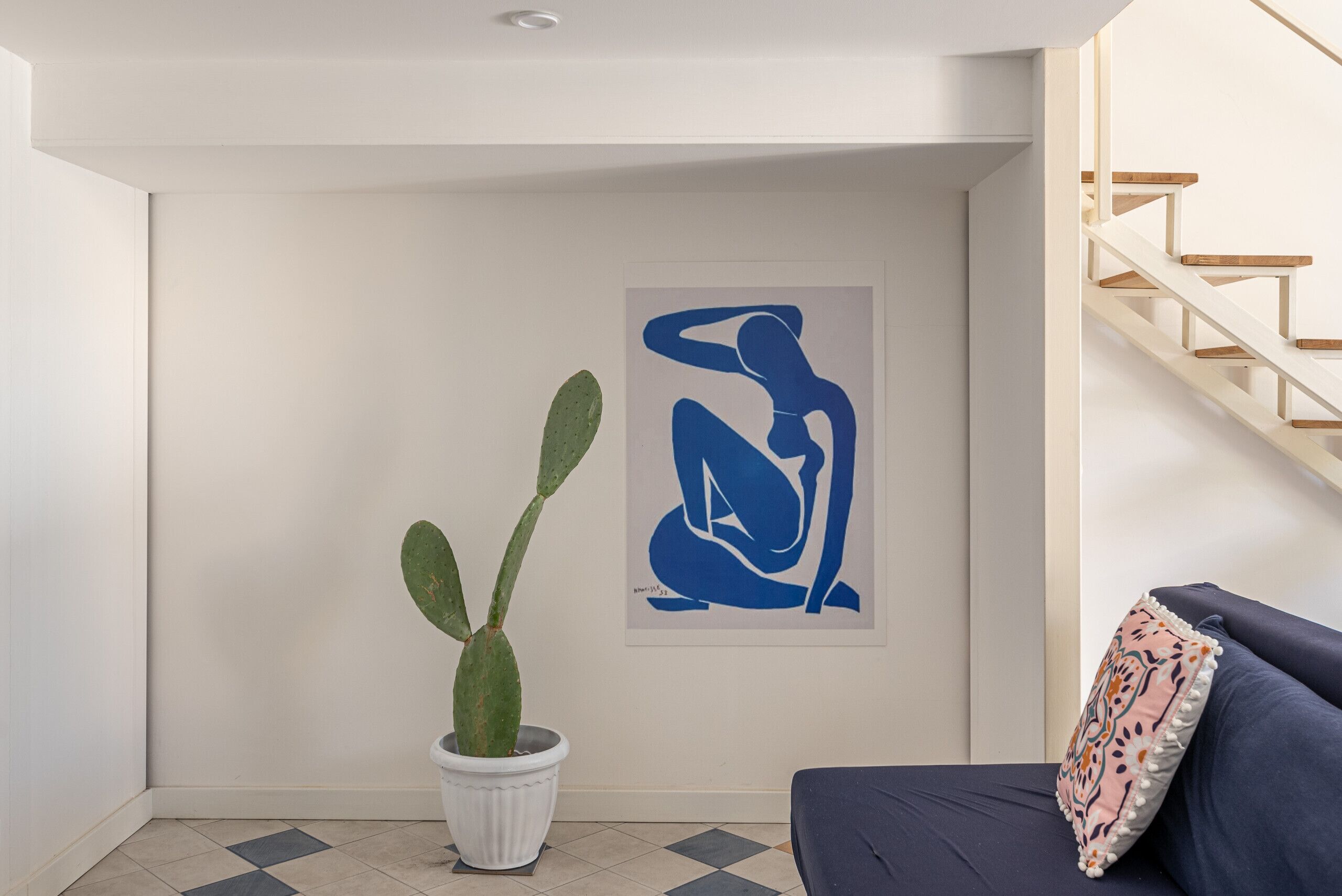 Un intérieur moderne agrémenté d’un cactus, d’un tableau abstrait bleu et d’un escalier.