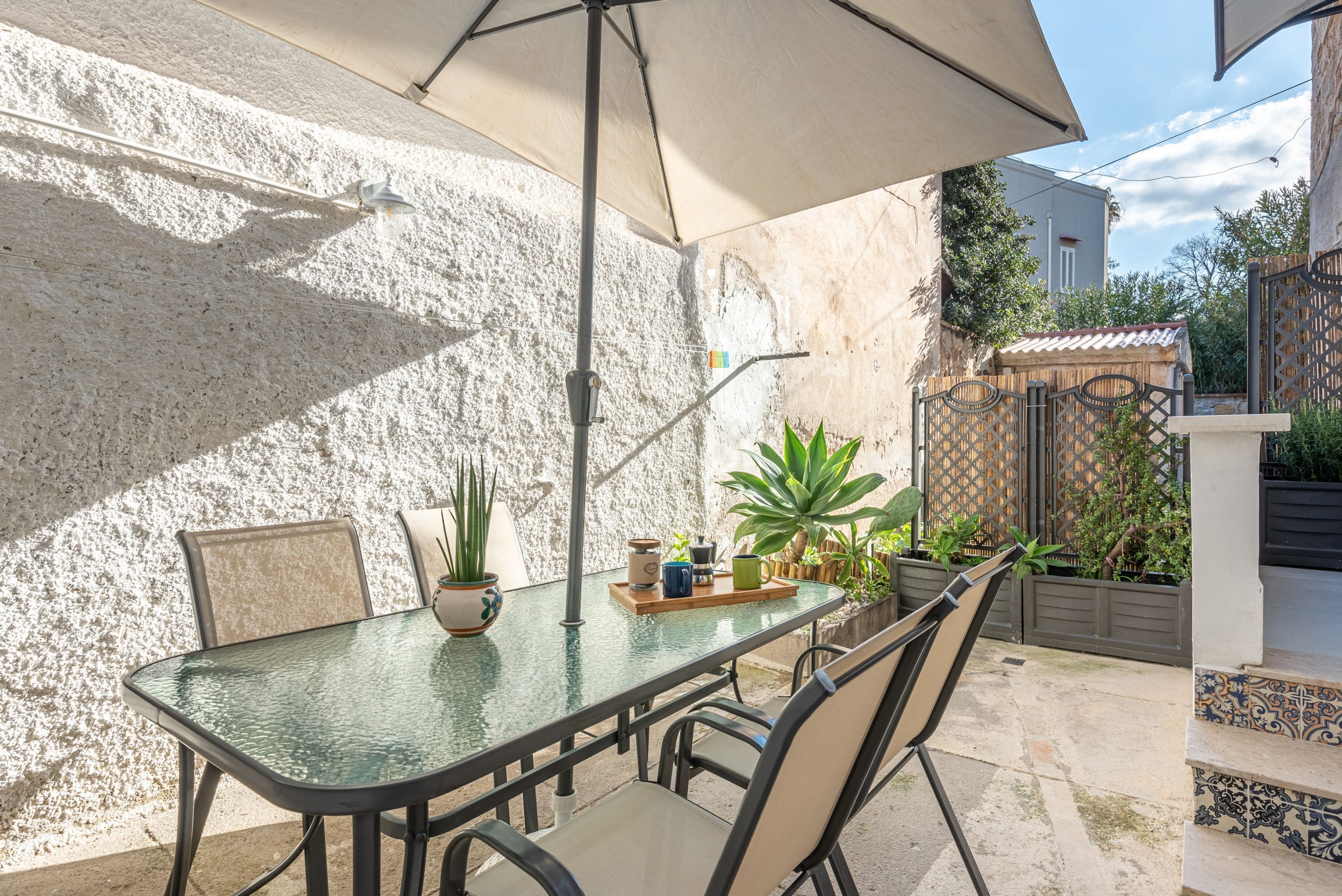 An outdoor patio with a glass table, chairs, a potted plant, and a decorative fence.