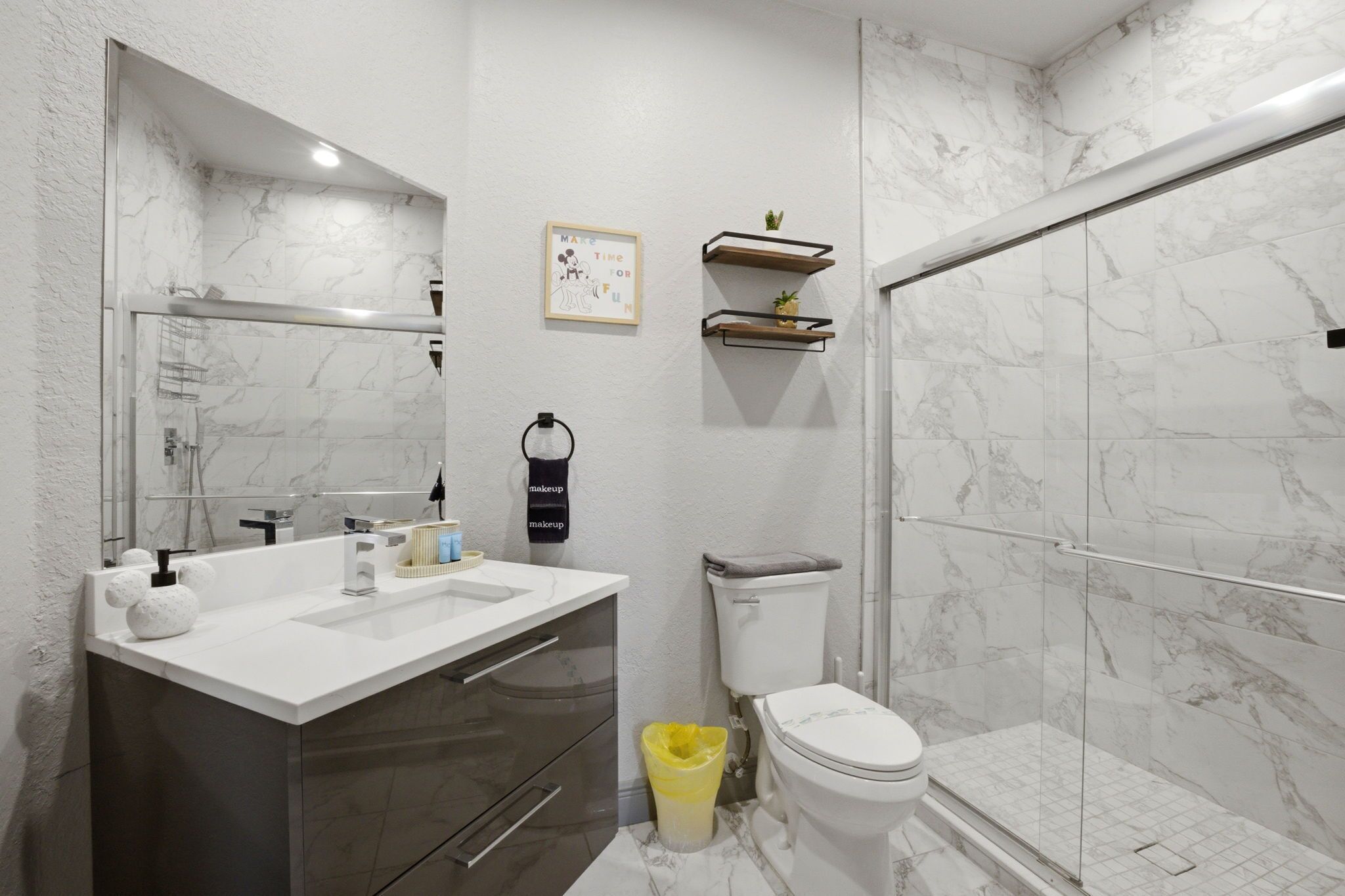 A modern bathroom with a marble sink, a toilet, a shower enclosure, and a vanity with drawers.