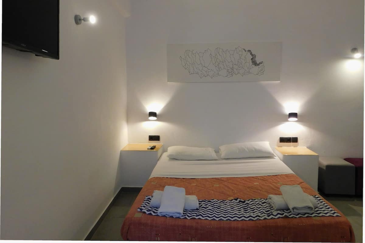 Une chambre d’hôtel comprenant un lit, deux tables de chevet, un téléviseur à écran plat fixé au mur et un luminaire mural.