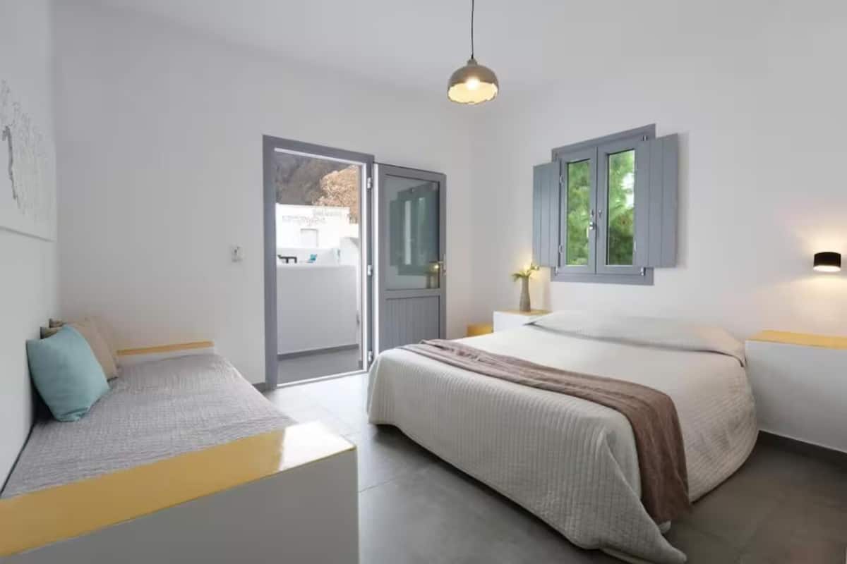 Une chambre à coucher comprenant un lit, des tables de chevet, un banc et une porte donnant sur un espace extérieur.
