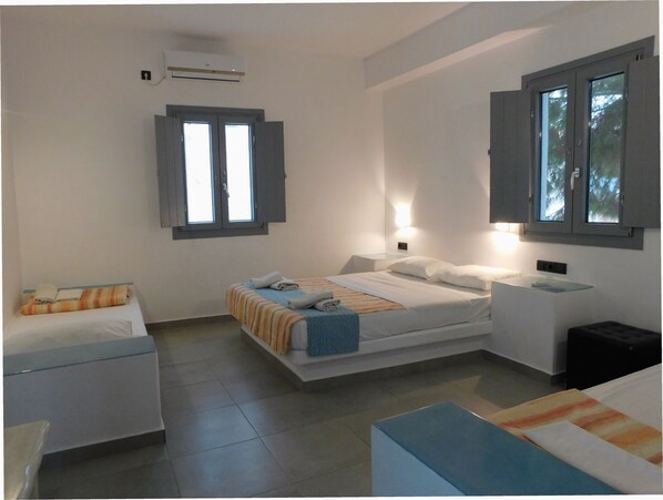 A hotel room with a bed, bedside tables, a small seating area, and a window with curtains. - Aegean Studios Perissa (Santorini)