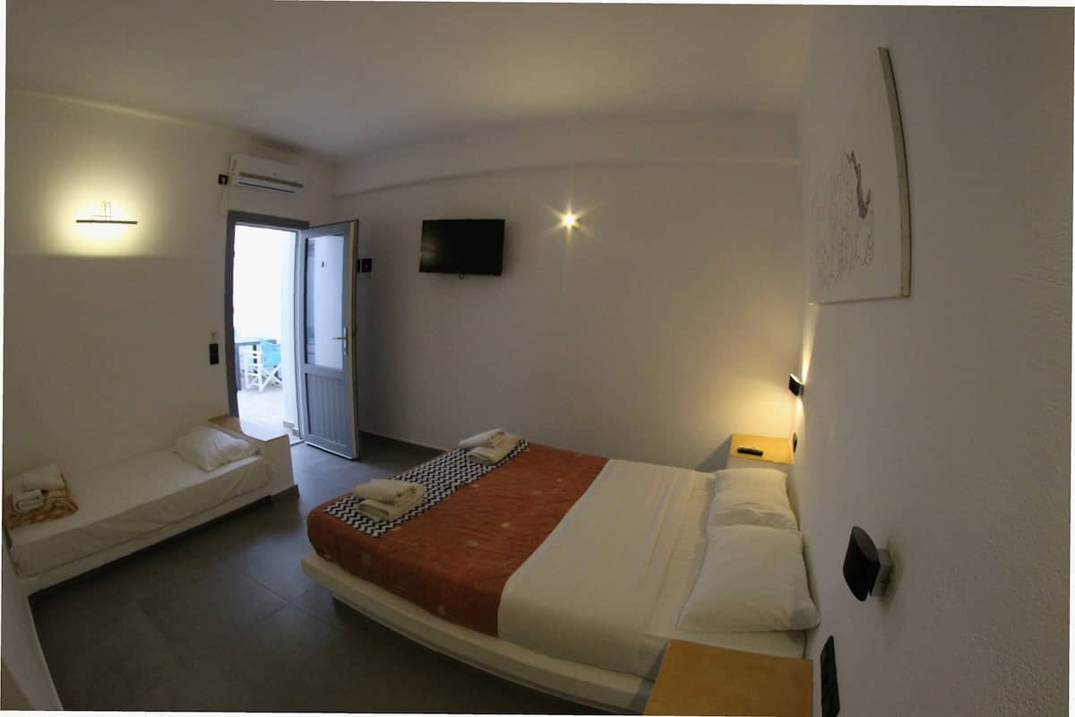 Une chambre d’hôtel avec un lit simple, un canapé-lit, une télévision à écran plat et une porte donnant sur un balcon.