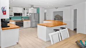 Una cocina moderna con armarios blancos, encimera de madera, electrodomésticos de acero inoxidable y una zona de comedor con mesa y sillas de madera.