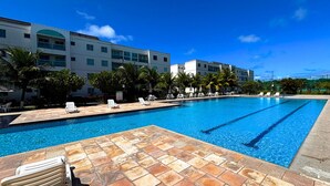 Piscina com espreguiçadeiras e palmeiras, cercada por um edifício com varandas múltiplas.