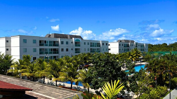 Um hotel moderno com vários andares, piscina e paisagismo tropical exuberante.