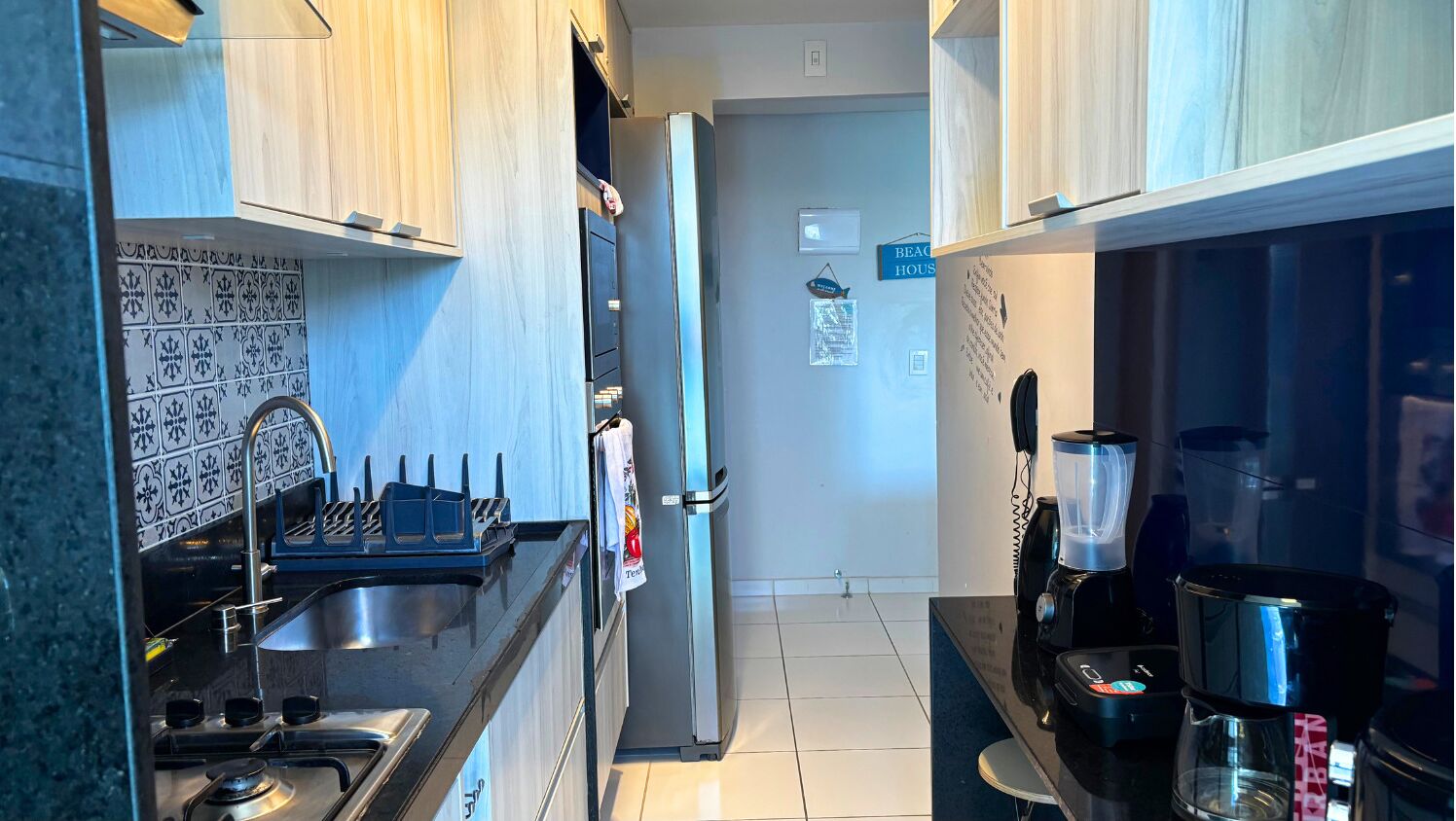 Cocina compacta con estufa, lavamanos y refrigerador. Hay una cafetera y una licuadora en la encimera.