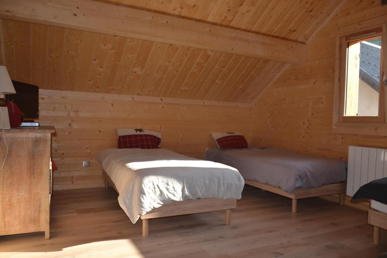 Une cabine équipée de deux lits en bois, d’une commode et d’une fenêtre laissant entrer la lumière naturelle.