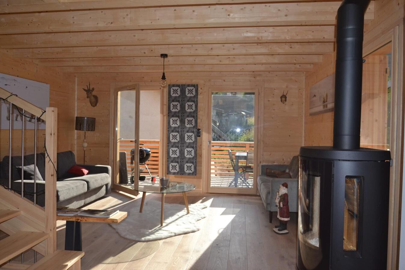 A cozy cabin interior with a wooden interior, a glass table, a sofa, and a black wood-burning stove.
