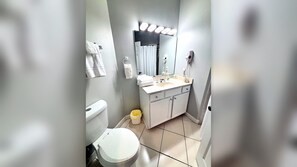 A bathroom with a toilet, sink, mirror, and a trash bin.
