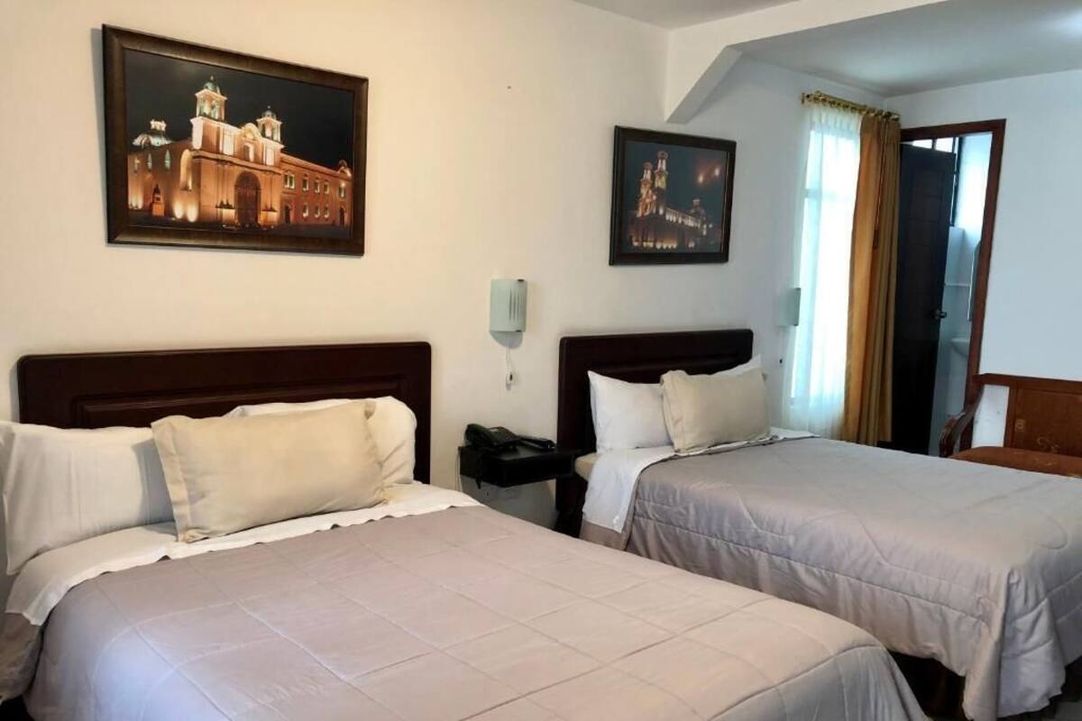 A hotel room with two beds, a nightstand, a telephone, and two framed pictures on the wall.