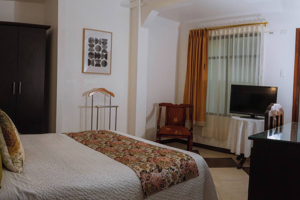 A hotel room with a bed, a wardrobe, a television, and a desk.