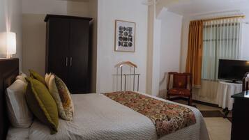 Una habitación de hotel con una cama, un armario, un televisor y un escritorio.