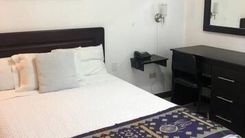 Quarto de hotel com uma cama, uma escrivaninha, uma cadeira, um telefone e um quadro na parede.