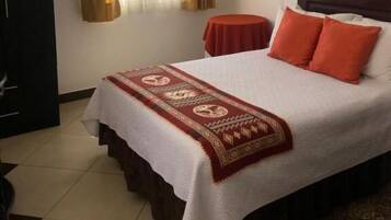 Ein Hotelzimmer mit einem Bett, einem kleinen Tisch, einem Kleiderschrank, einem Fenster mit Vorhängen und einem an der Wand hängenden Bild.