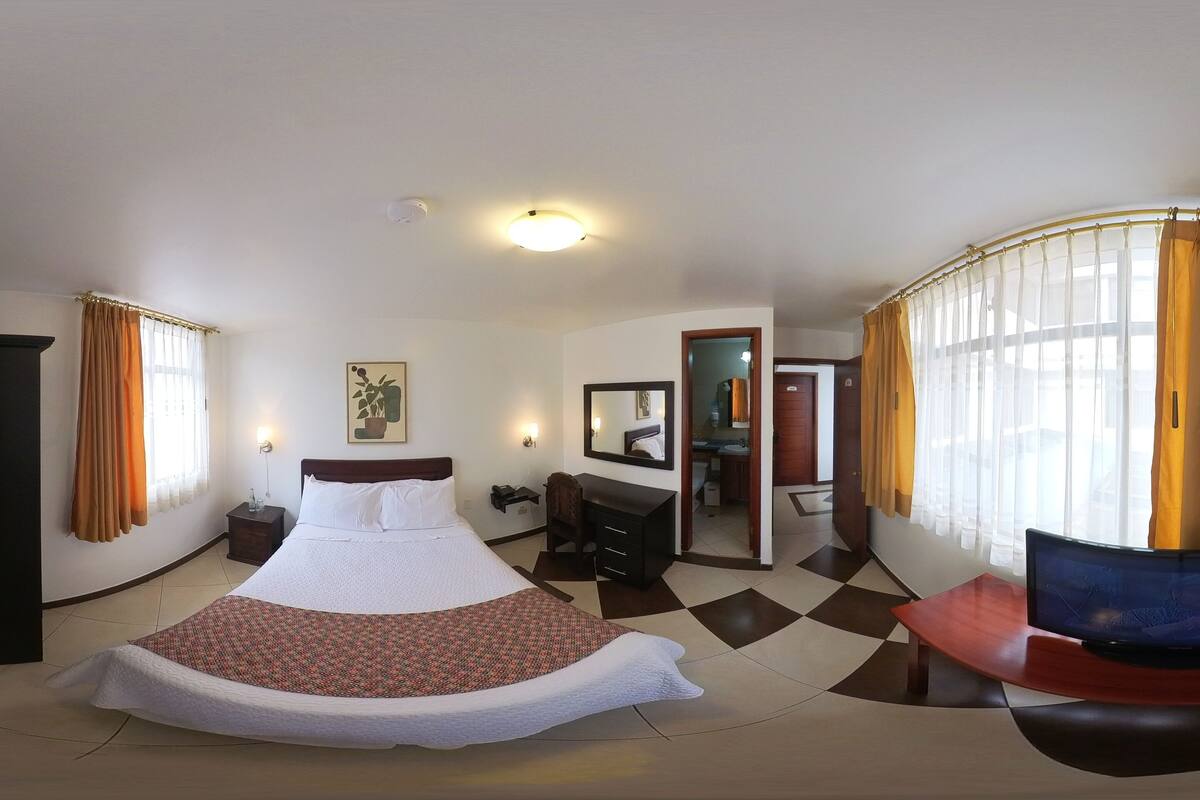 A hotel room with a large bed, a wardrobe, a desk, and a mirror.