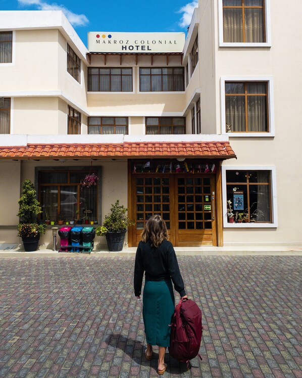 Exterior del hotel MakroZ Colonial, con techo de tejas, plantas en macetas y un cartel.