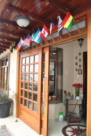 Una puerta de madera con paneles de vidrio, una planta en maceta y una pequeña mesa con un pulverizador y un florero. Banderines cuelgan sobre la puerta.