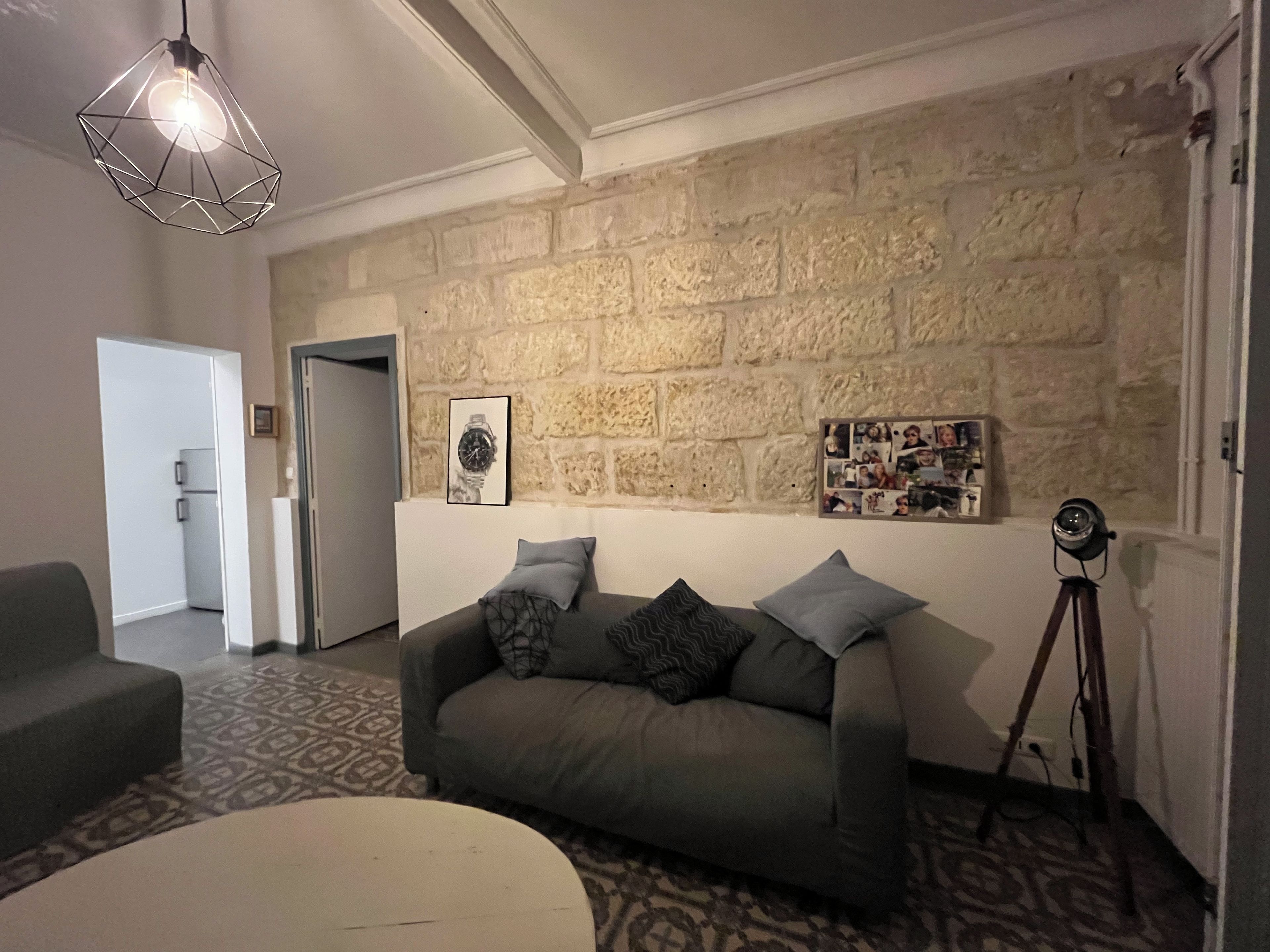 Een woonkamer met een stenen muur, een bank, een tapijtendeken, een statief en een hanglamp.