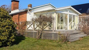 Une maison moderne dotée d’une véranda en verre, d’une cheminée en briques et d’une terrasse en bois.