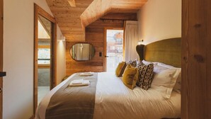 Un dormitorio con techo de madera, una cama con almohadas blancas y estampadas, un espejo redondo y vistas a un edificio.