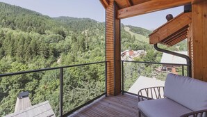 Un balcón con piso de madera y baranda metálica, con vista a un valle boscoso.