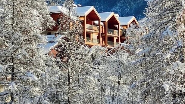 Una cabaña rodeada de múltiples cabañas de madera, con árboles nevados y montañas al fondo.
