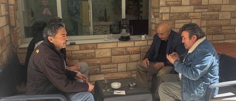 Four men seated at an outdoor table with a brick wall and window in the background.