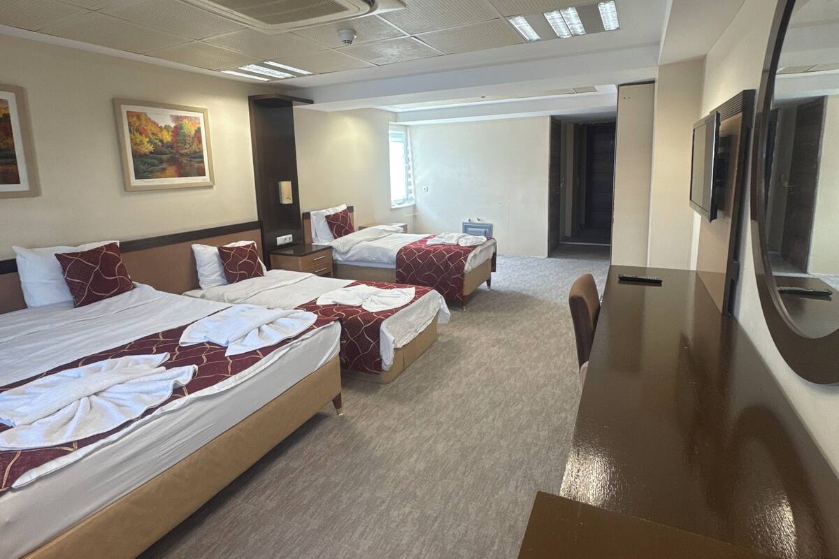 A hotel room with four beds, a large mirror, and a desk.