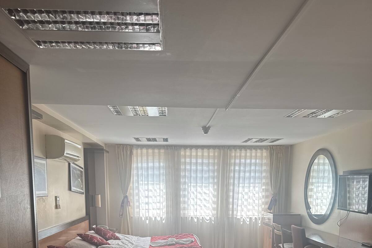A hotel room with two beds, a desk, a TV, and a large window with curtains.