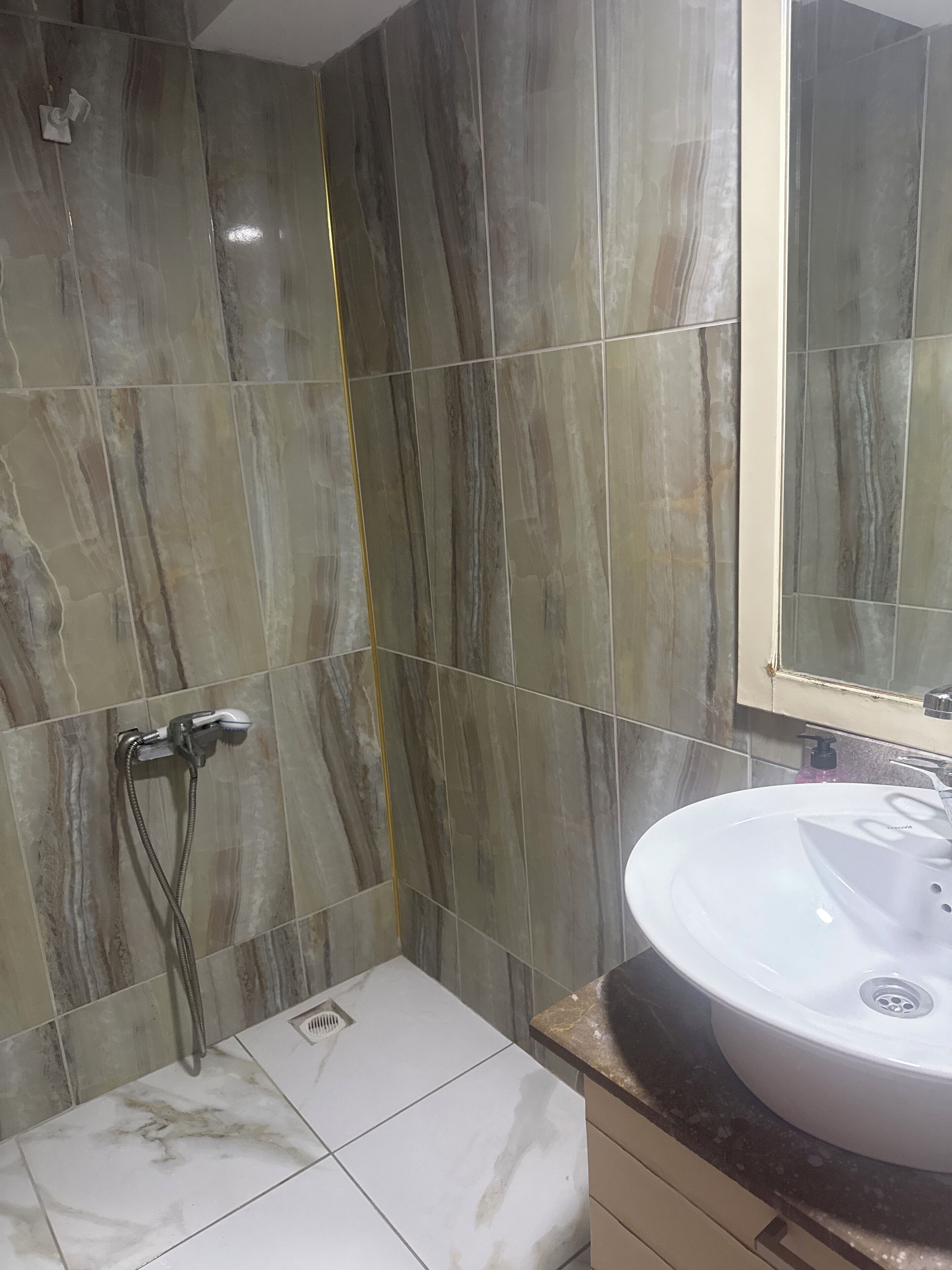 Un baño con baldosas de mármol, un lavamanos blanco y una ducha con cabezal de ducha de mano.