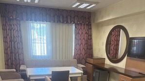A hotel room with a sofa, a dining table with chairs, a TV, a mirror, and a carpeted floor. - Edremit Körfez Turizm (Edremit)