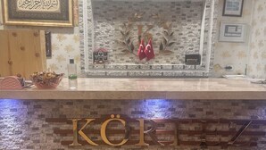 A reception area with a stone wall, a clock, framed calligraphy, and flags. - Edremit Körfez Turizm (Edremit)