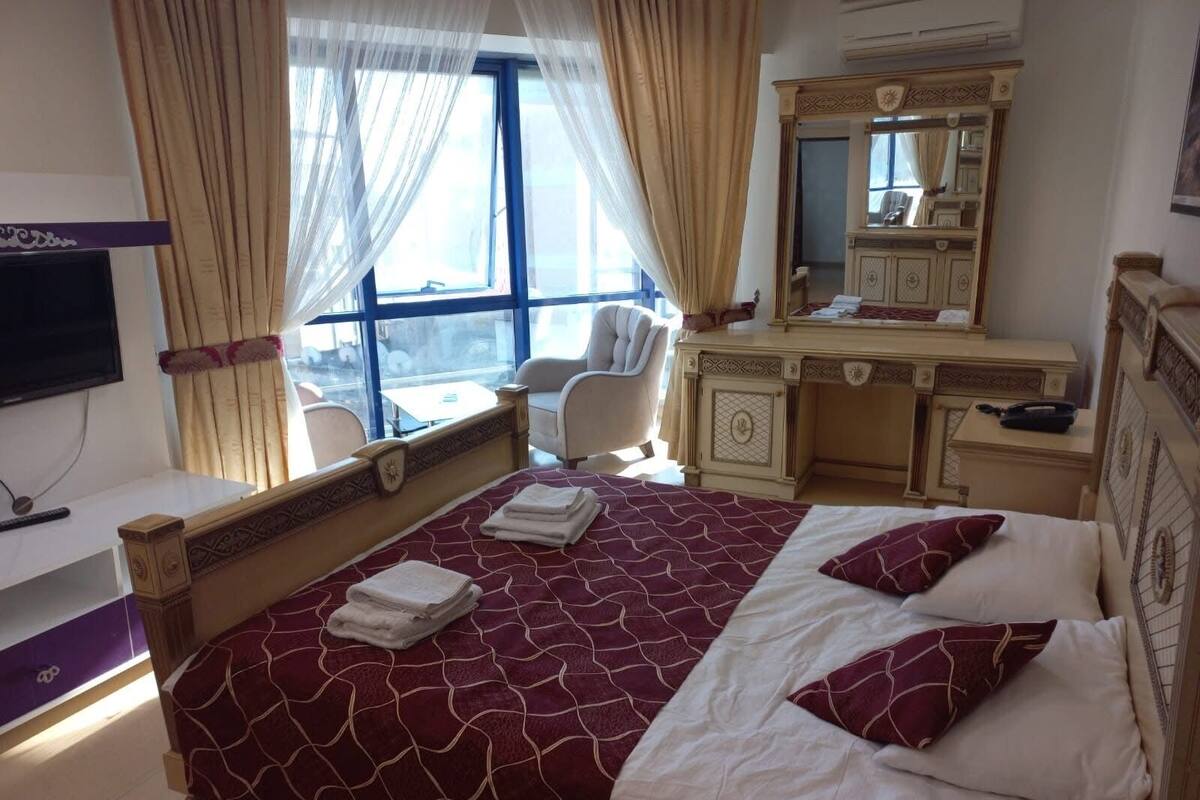 A hotel room with a large bed, a desk, a chair, a television, and a window with curtains.