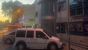 A white SUV parked on a cobblestone street in front of a building with a balcony and a flag. - Edremit Körfez Turizm (Edremit)