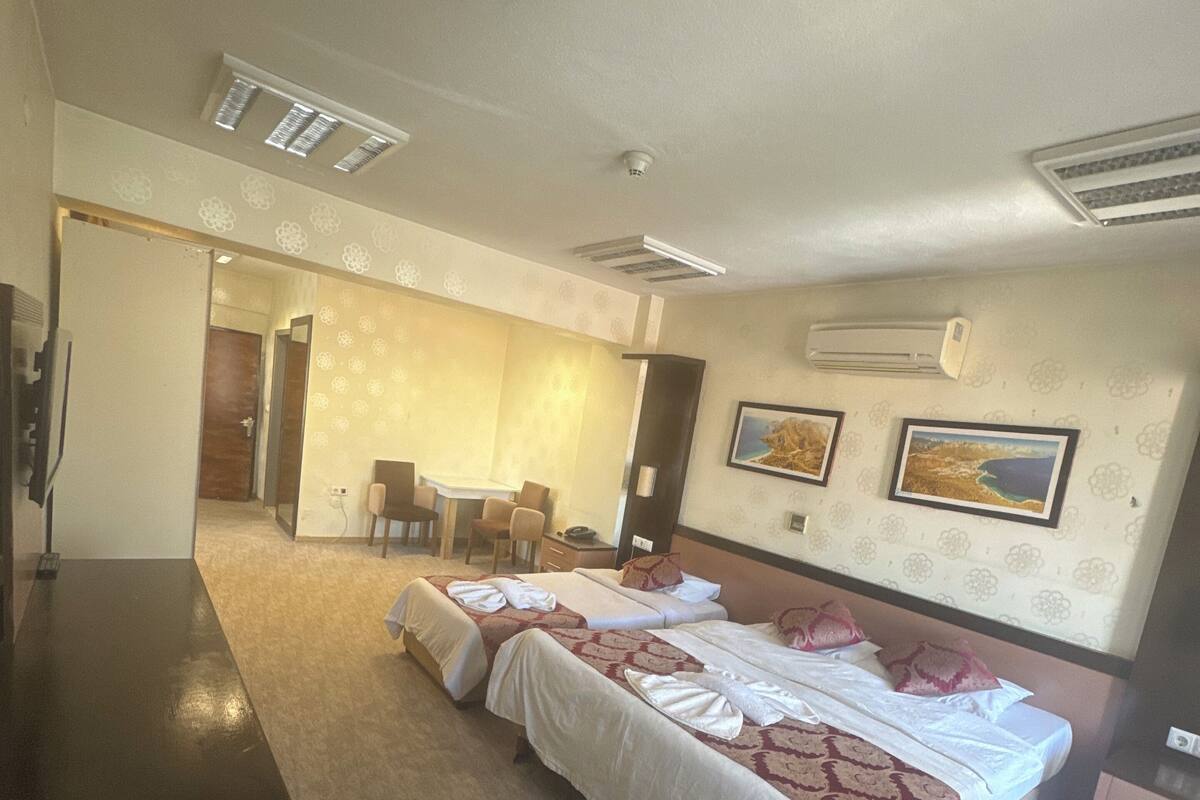 A hotel room with a large bed, a desk, and a chair. There are two air conditioning units on the wall.