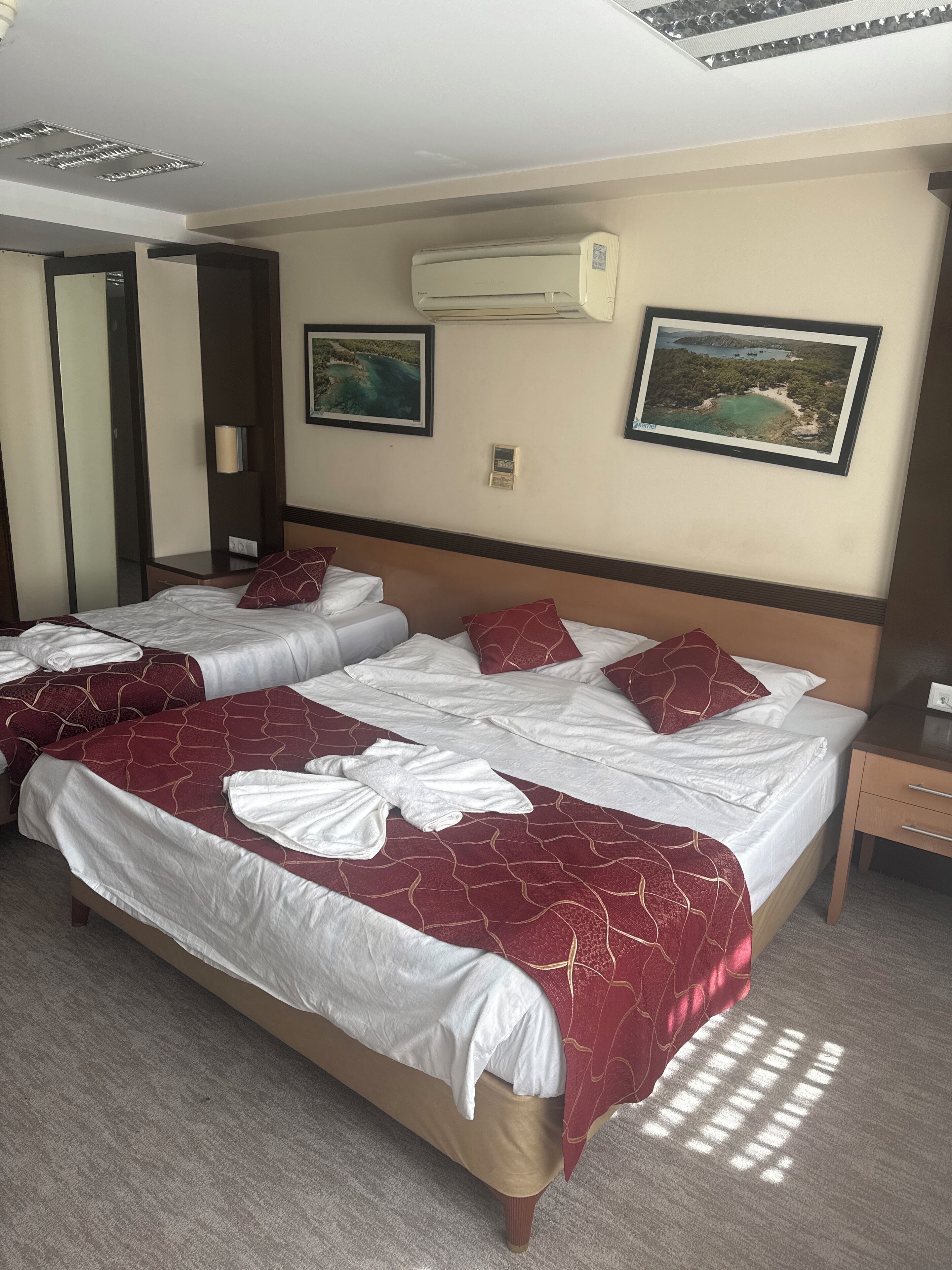 A hotel room with two beds, a wall-mounted air conditioner, and two framed pictures.