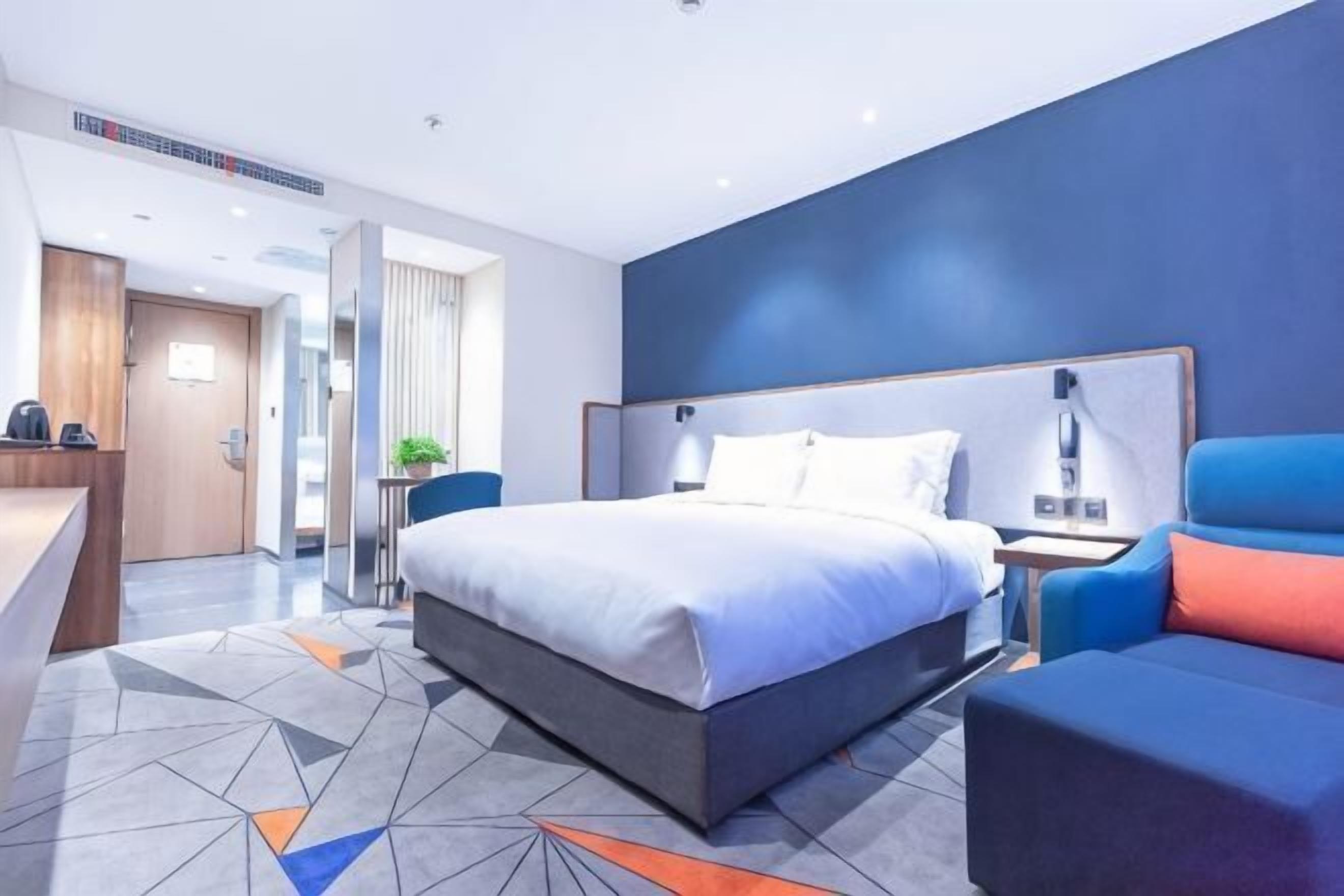 A modern hotel room with a large bed, a desk, and a seating area.
