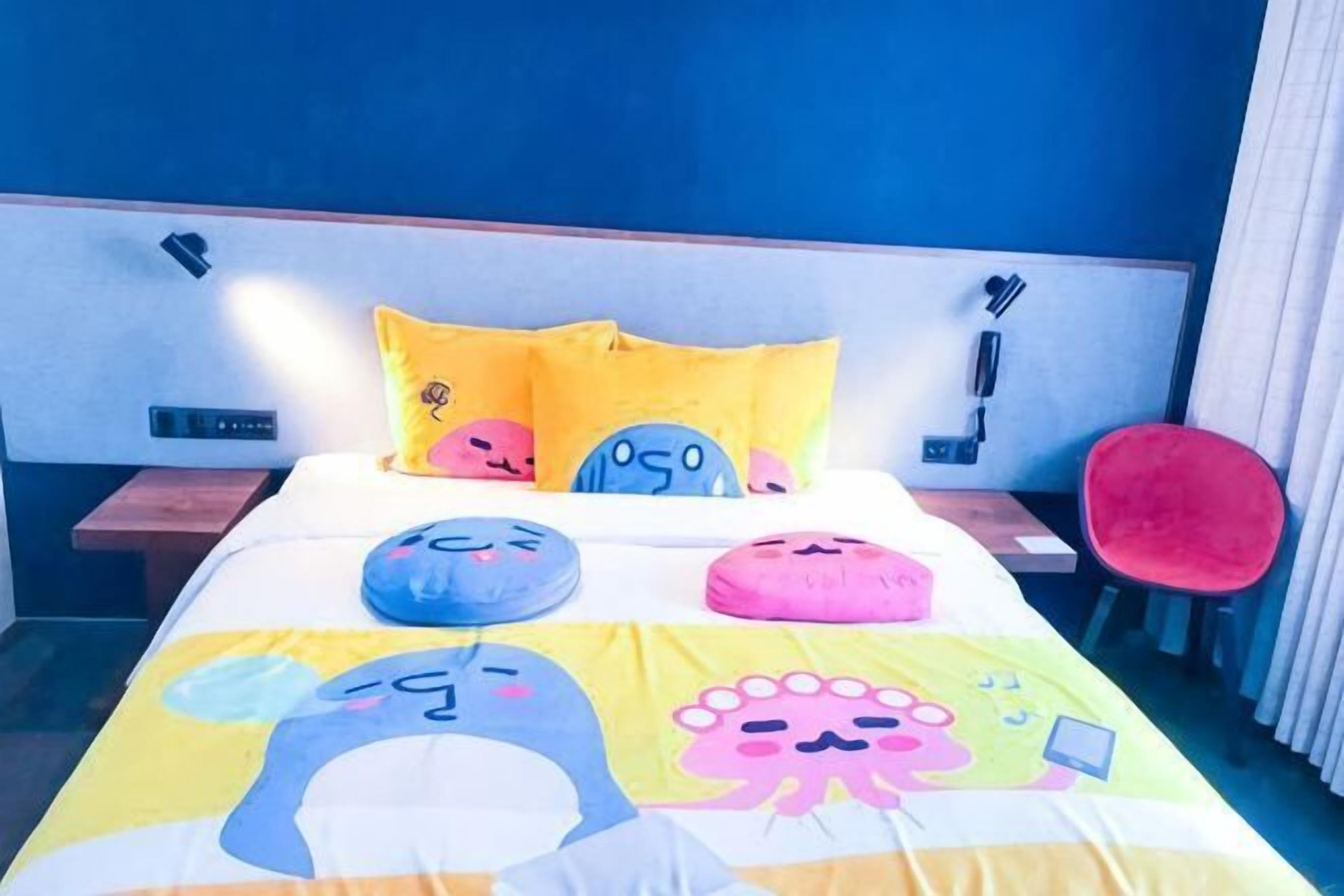 A bed with colorful pillows, a red chair, and a modern headboard.
