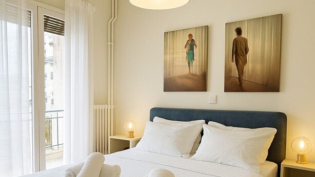 Un dormitorio bien iluminado con una cama grande, dos mesitas de noche con lámparas y una obra de arte en la pared.