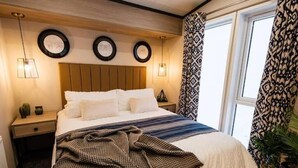 A neatly made bed with a checkered blanket, a bedside lamp, and a nightstand with a vase. - Relax at Riverwood (Arbroath)