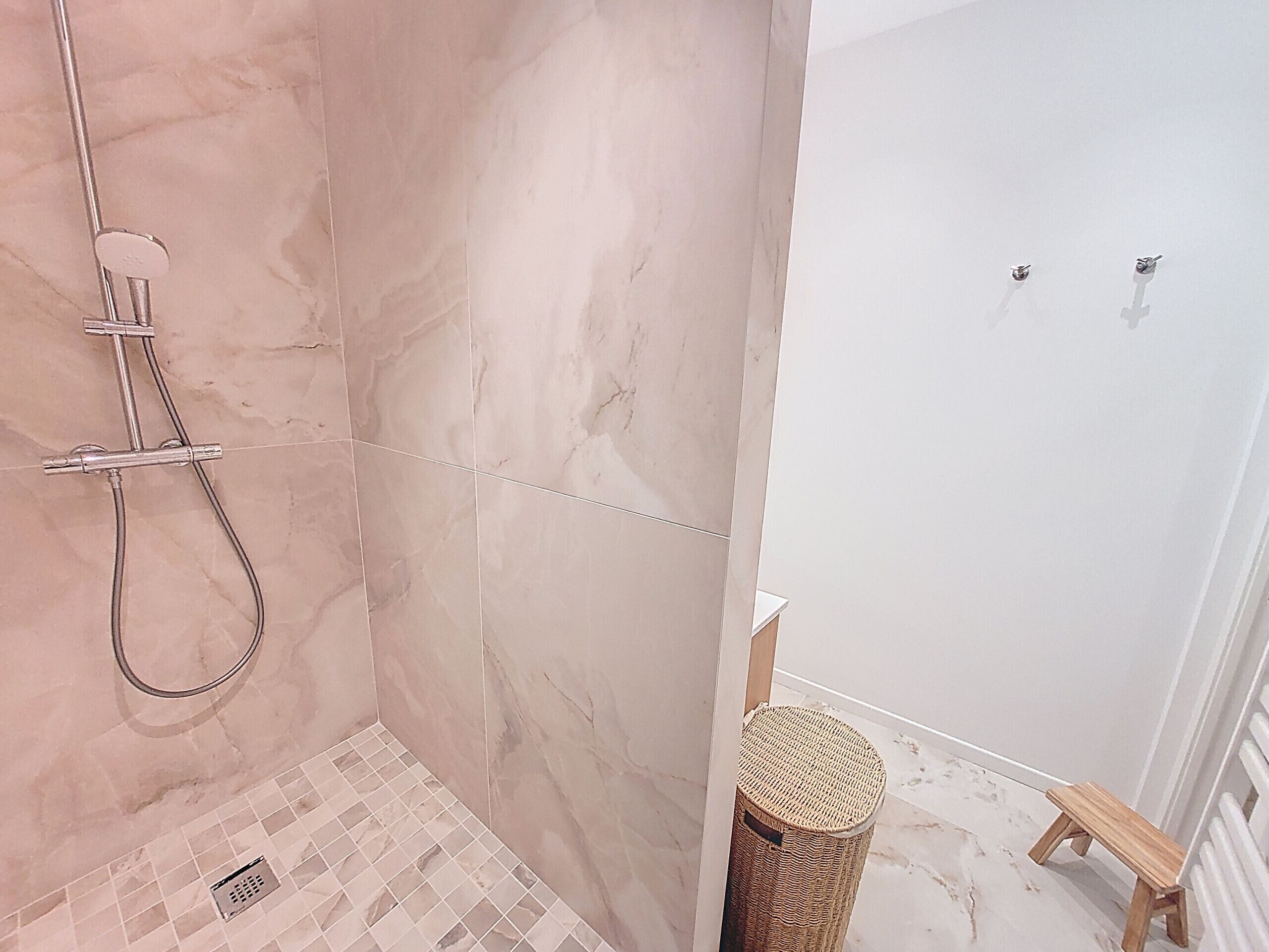 A bathroom with a shower, a small wooden stool, and a wicker basket.