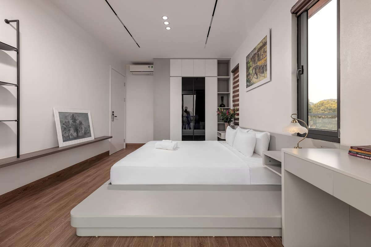 A modern bedroom with a bed, built-in shelving, a desk, and a window with a view.