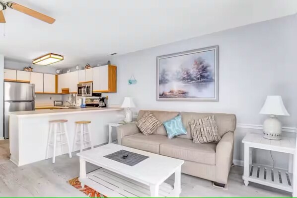 Una sala de estar moderna con un sofá, una mesa de centro y una cocina al fondo.