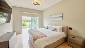 Un dormitorio con cama, televisión, mesita de noche y puerta corrediza a un balcón.